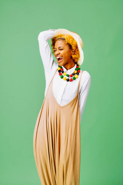 Fun portrait of a stylish girl laughing and holding hat Fun portrait of a stylish girl laughing in front of a green background huge black woman pictures stock pictures, royalty-free photos & images
