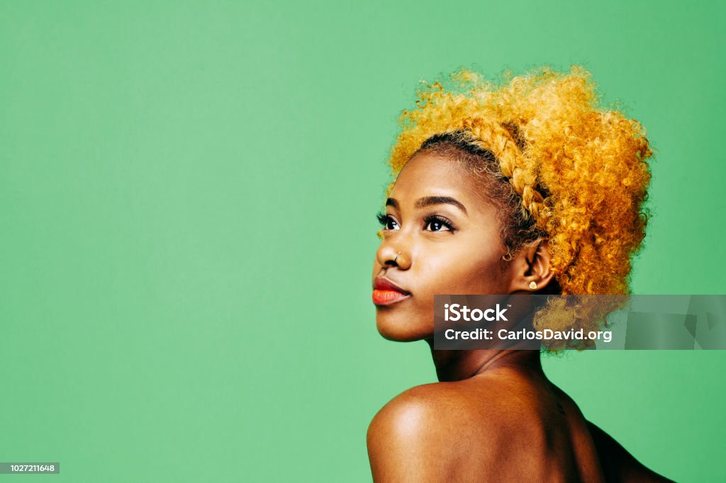 Beautiful young girl with bleached curly hair and bare shoulder looking up Beautiful young girl with bleached curly hair and bare shoulder looking up, in front of a green background Women Stock Photo