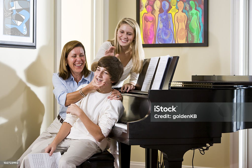 Família sentada no piano banco, filho de mãe Travessura - Foto de stock de 14-15 Anos royalty-free