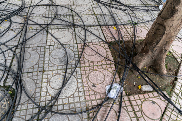 шнур питания и кабельная мощность запутались на тротуаре, полу и круге дренажного шланга и корня дерева. - mishmash стоковые фото и изображения