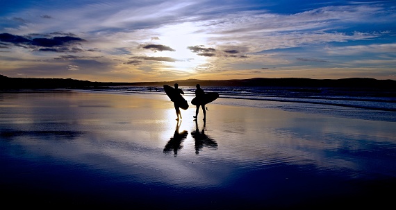 Surfers walking across a beach at sunset in St Ives Bay Cornwall