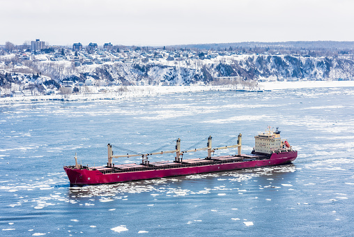 A large cargo ship making its way through the ice-covered water surface of the Saint Lawrence River in Quebec, Canada.