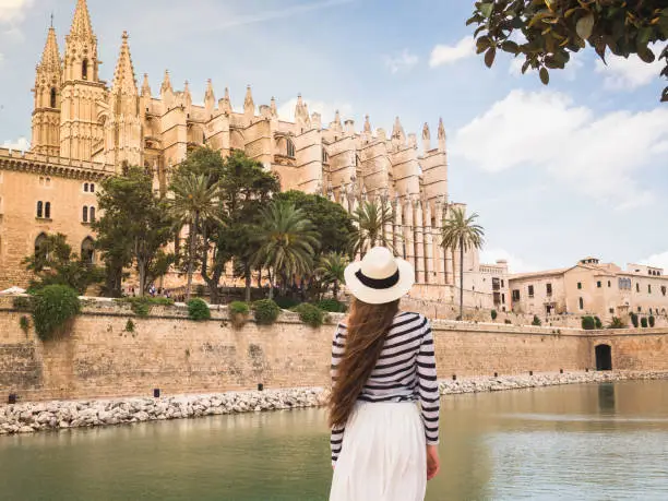 Stylish, beautiful woman on the background of palm trees, river and historical buildings. Spain, Palma de Mallorca