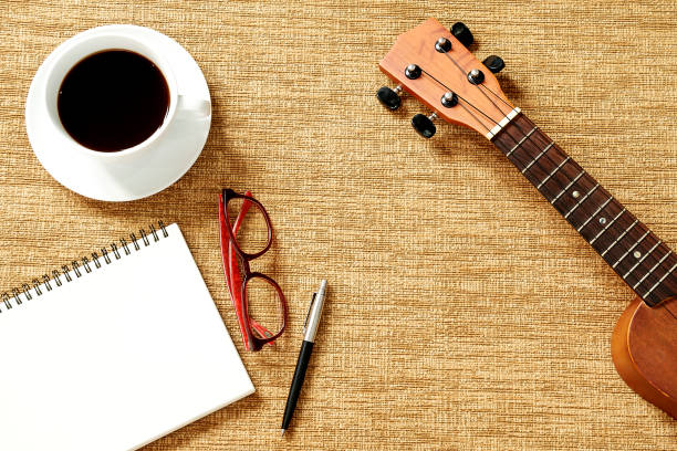 istock Top view of ukulele, notebook, pen, coffee cup and glasses on brown background 1027257206