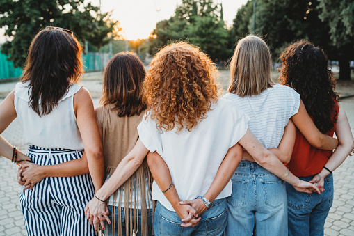 Grupo de amigos de las mujeres agarrados de la mano juntos contra la puesta de sol photo