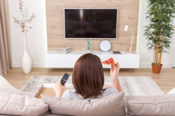 istock Single woman eating pizza and watching tv 1027272502