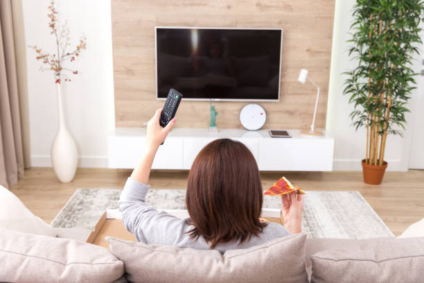 istock Single woman eating pizza and watching tv 1027272582