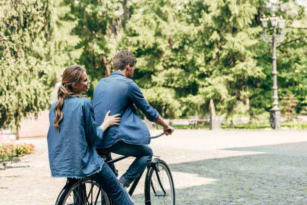 istock beautiful young couple riding bicycle together at park 1027284432