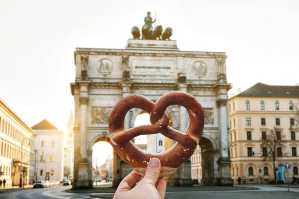 A girl or a young woman is holding a traditional German pretzel The girl is holding a delicious traditional German pretzel in the hand against the backdrop of the Victory Gate triumphal arch Siegestor in Munich. Germany münchen stock pictures, royalty-free photos & images