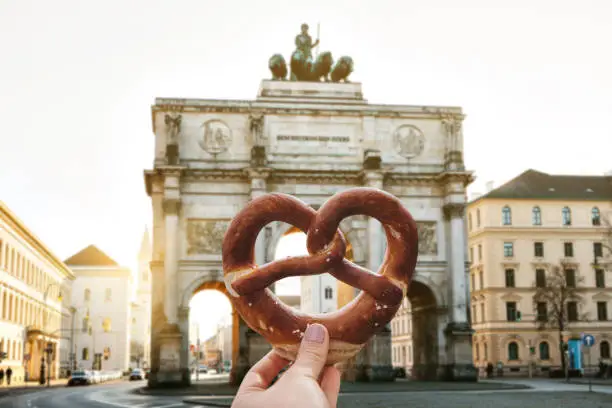 The girl is holding a delicious traditional German pretzel in the hand against the backdrop of the Victory Gate triumphal arch Siegestor in Munich. Germany