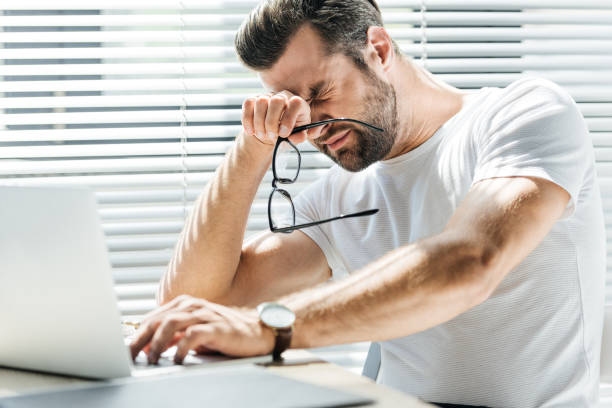 istock tired man holding eyeglasses while sitting at workplace with laptop 1027310202