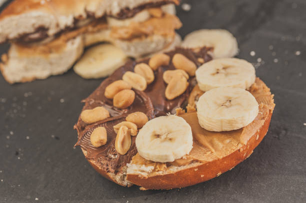 petit déjeuner savoureux : bagel avec du beurre d’arachide, tranches de banane, cacahuètes salées au chocolat d’ant - wood ant photos et images de collection