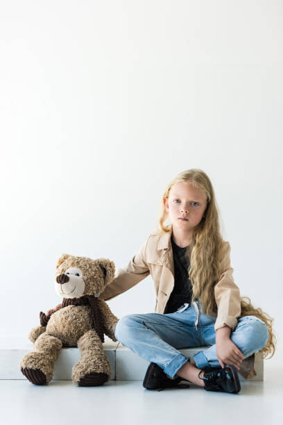 istock beautiful child looking at camera while sitting with teddy bear on white 1027321700