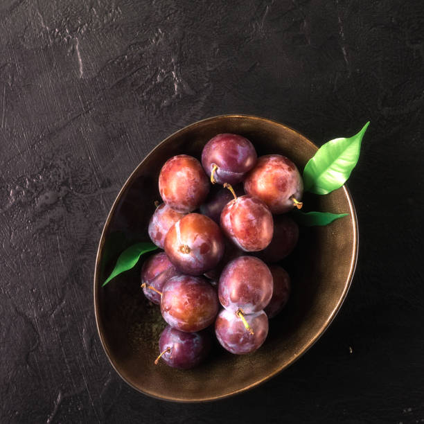 istock Whole fresh red violet blue plums and slices cut with knife in bowl on kitchen table 1027342076
