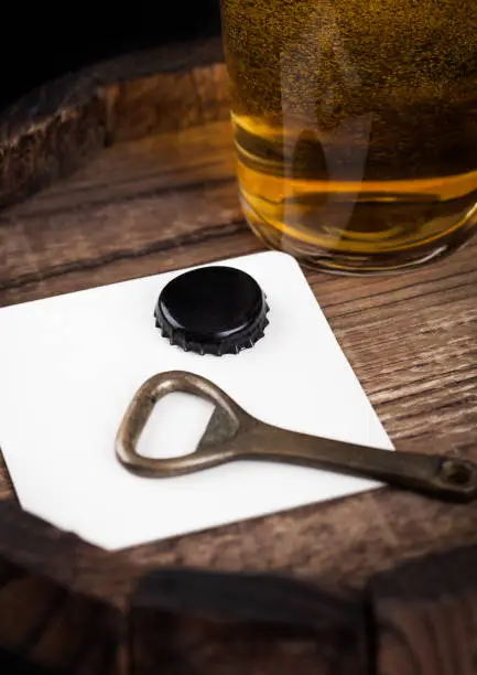 Beer coaster with bottle top and opener and glass of beer on top of wood barrel.