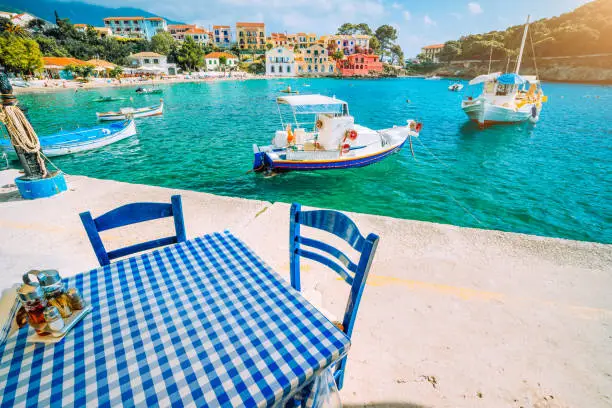 Traditional Greek restaurant with blue and white table and chairs at the sea coast of Assos village. Azure water, sunshine, summer feeling summer vacation.