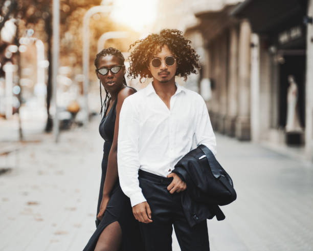 Fancy interracial couple on a street of Barcelona Interracial couple on the city street: a young charming African girl with braids, in a black dress and an asian guy with curly hair, in sunglasses holding a jacket of his suit; sunny autumn day hot filipina women stock pictures, royalty-free photos & images