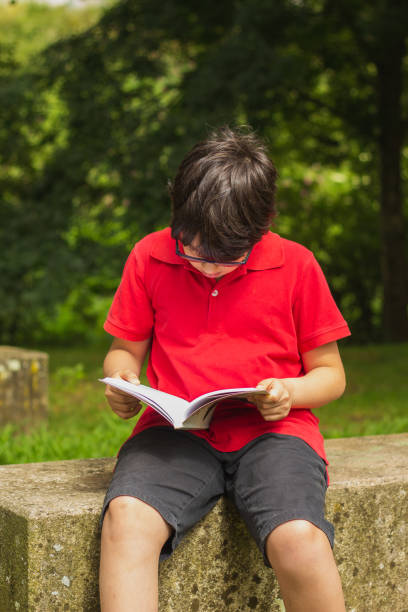 istock Cute boy reading a book at the park 1027409560