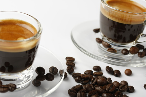 Top view of brewed espresso in a cup at whole roasted coffee beans background, invigorating morning drink