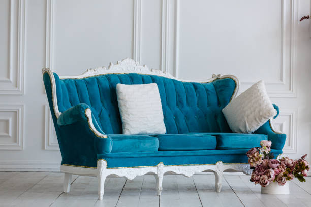 istock Classic blue sofa in a luxurious white room. artificial fireplace. on the fireplace is a mirror in the frame. the room is decorated with flowers. in the room hangs a chic chandelier 1027521746
