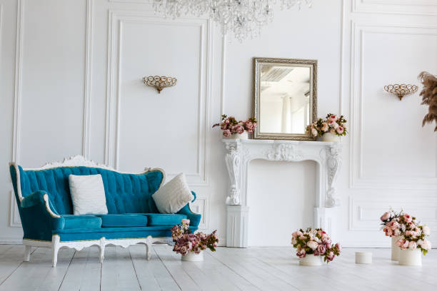 istock Classic blue sofa in a luxurious white room. artificial fireplace. on the fireplace is a mirror in the frame. the room is decorated with flowers. in the room hangs a chic chandelier 1027521760