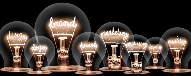 Photo of light bulbs with shining fibres in shape of BRAND concept related words isolated on black background