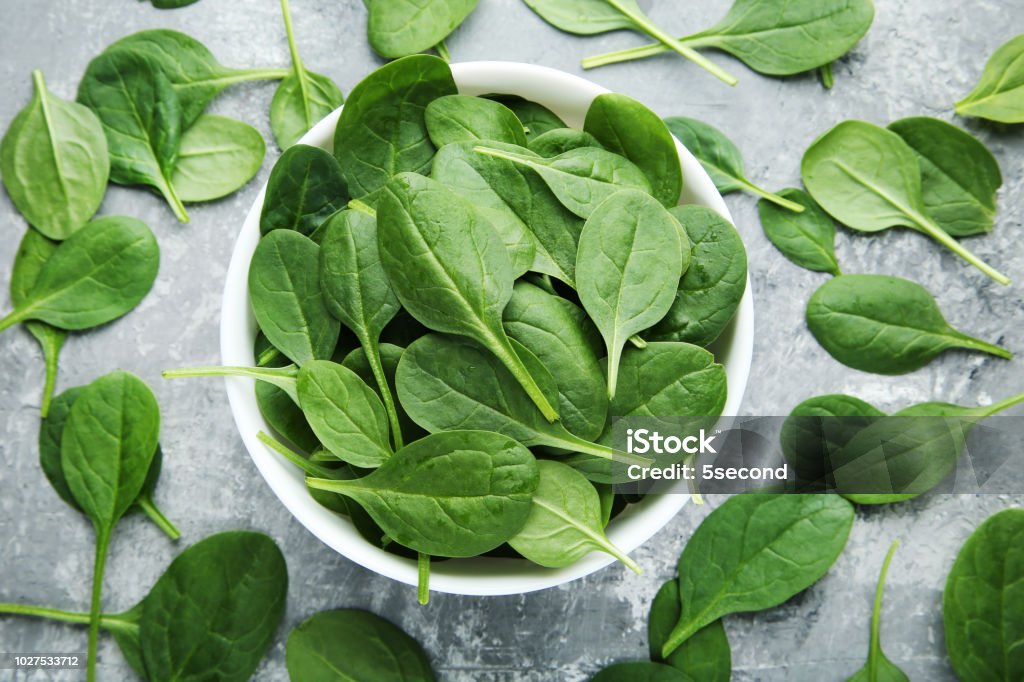 Spinach leafs in bowl on grey wooden table Spinach Stock Photo