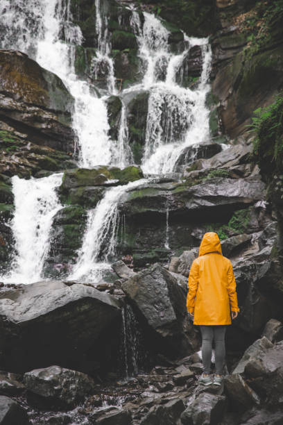 istock woman standing in yellow raincoat and looking at waterfall 1027542924