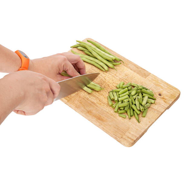 Slicing fresh green beans on a cutting board on a table, white isolated background