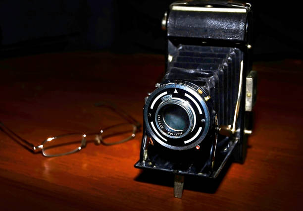 istock Vintage old photographic camera and glasses. Spot lighting, black background 1027549932