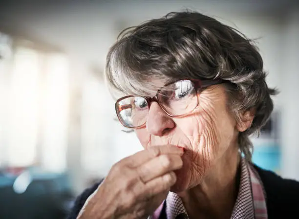 Photo of Senior woman takes a bite of something and smiles, her eyes twinkling.