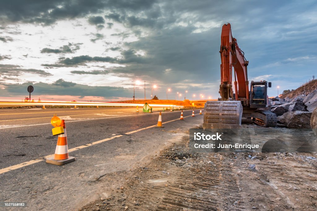 Works of extension of a road with excavator and delimited by safety cones Works of extension of a road Road Construction Stock Photo