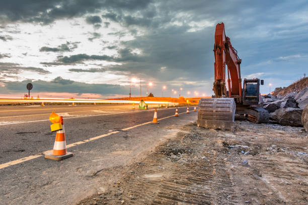 Works of extension of a road with excavator and delimited by safety cones Works of extension of a road road construction photos stock pictures, royalty-free photos & images