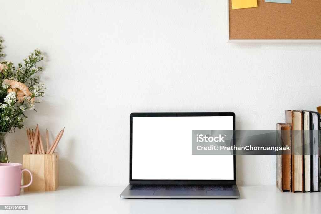 Workspace Mock up laptop and table of creative desktop of female designer with nobody. Flower bouquet and coffee mug with book. Desk Stock Photo