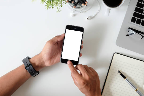 istock Top view office desk with mockup smartphone on hands with empty display screen. 1027575246
