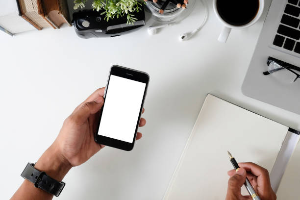 istock Top view office desk with mockup smartphone on hands with empty display screen. 1027579168