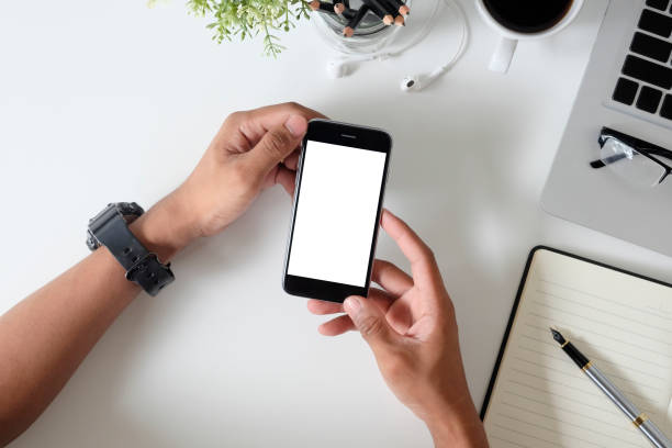 istock Top view office desk with mockup smartphone on hands with empty display screen. 1027581922