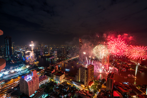 Bangkok, Thailand - December  31, 2017: Bangkok  view showing Bangkok city, houses, buildings, river, bridge, trees and boats with fireworks on the background at night in the Lebua area