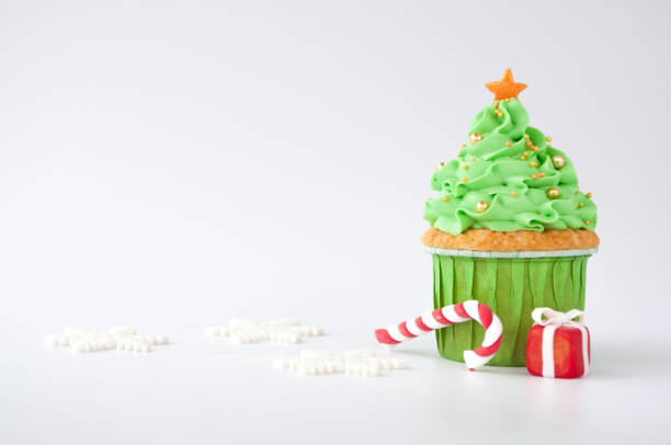 ano novo ou cupcake de natal verde com creme chantilly, decorado com uma árvore de natal, pirulito, um flocos de neve, uma caixa vermelha, bolas de confeitaria de ouro sobre fundo branco. - christmas desserts - fotografias e filmes do acervo