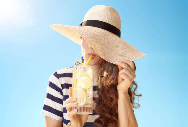 istock woman hiding behind straw hat and drinking refreshing cocktail 1027623810