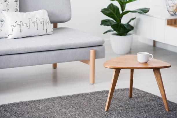istock Cup on a wooden coffee table and blurry foreground with graphic pillows on a gray sofa in a white living room interior 1027632512