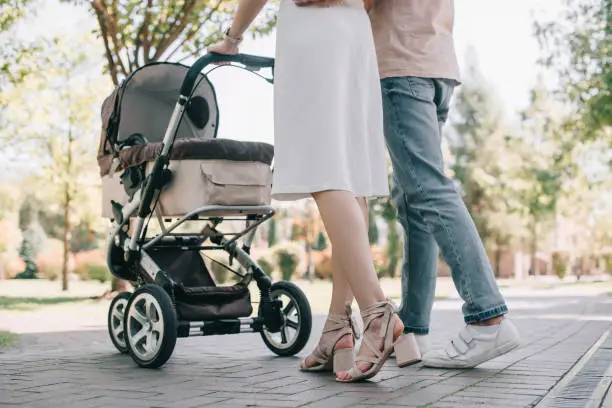 Photo of cropped image of parents walking with baby carriage in park