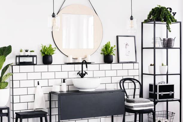istock Round mirror between plants in black and white bathroom interior with poster and chair. Real photo 1027646730
