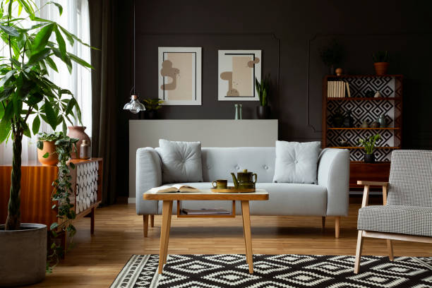 istock Wooden table and armchair on patterned carpet in retro flat interior with grey sofa and posters. Real photo 1027659892