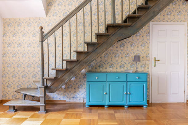 A light blue three door cabinet standing under gray staircase against a wall with flower wallpaper in a hall interior. Real photo. A light blue three door cabinet standing under gray staircase against a wall with flower wallpaper in a hall interior. Real photo. hampton virginia photos stock pictures, royalty-free photos & images