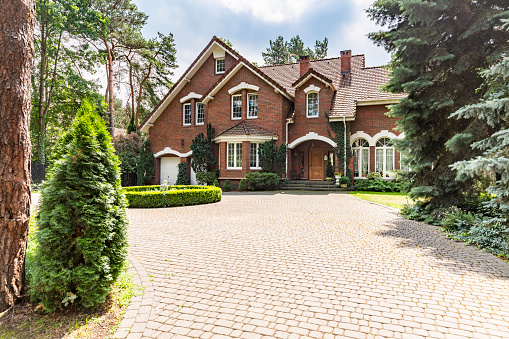 Large cobbled driveway in front of an impressive red brick English design mansion surrounded by old trees