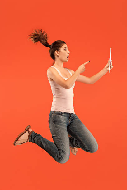 istock Image of young woman over blue background using laptop computer or tablet gadget while jumping 1027666364