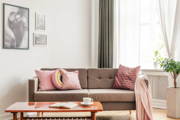 istock Wooden table in front of beige settee with pink pillows in flat interior with posters and plant. Real photo 1027666932