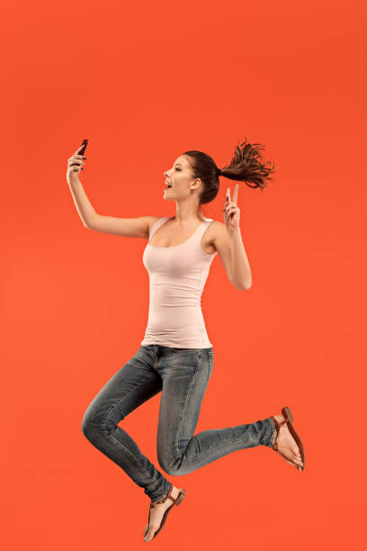 istock Image of young woman over blue background using laptop computer or tablet gadget while jumping 1027669554