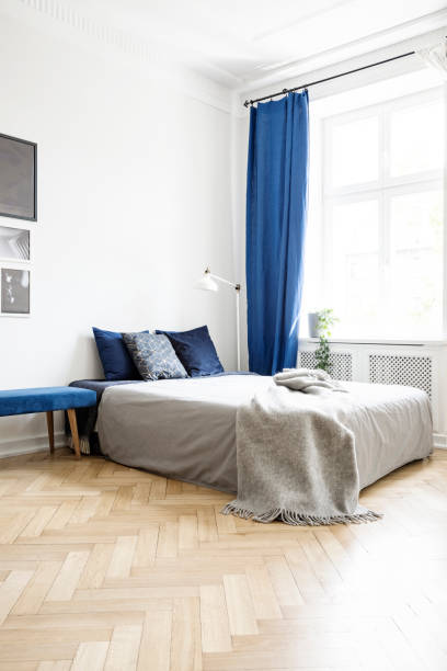 istock Grey blanket on bed in bright bedroom interior with lamp and navy blue drapes at window. Real photo 1027670156